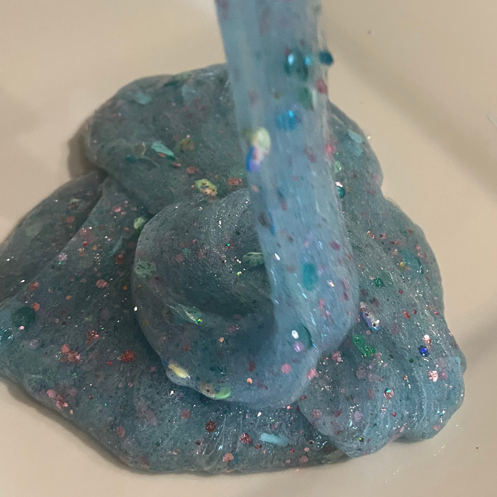 Mermaid Magic Slime Drizzle, Blue and glittery on a white surface.