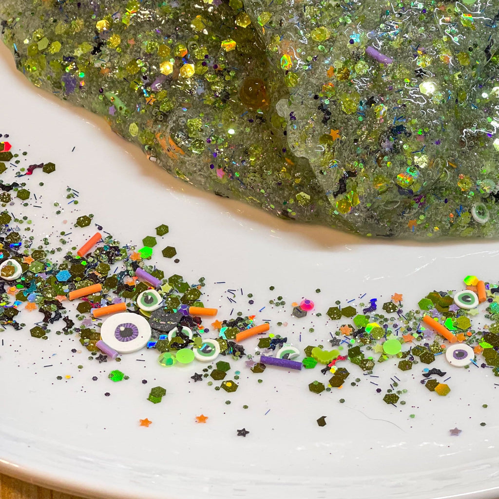 Witch's Brew (Glow-In-The-Dark) Slime Kit with slime on a white plate with confetti and other fixings that are mixed in the diy slime kit