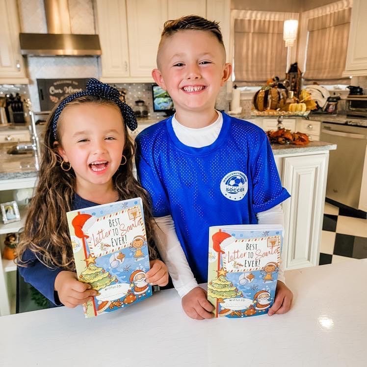 two kids smiling in a kitchen holding the best santa ever book