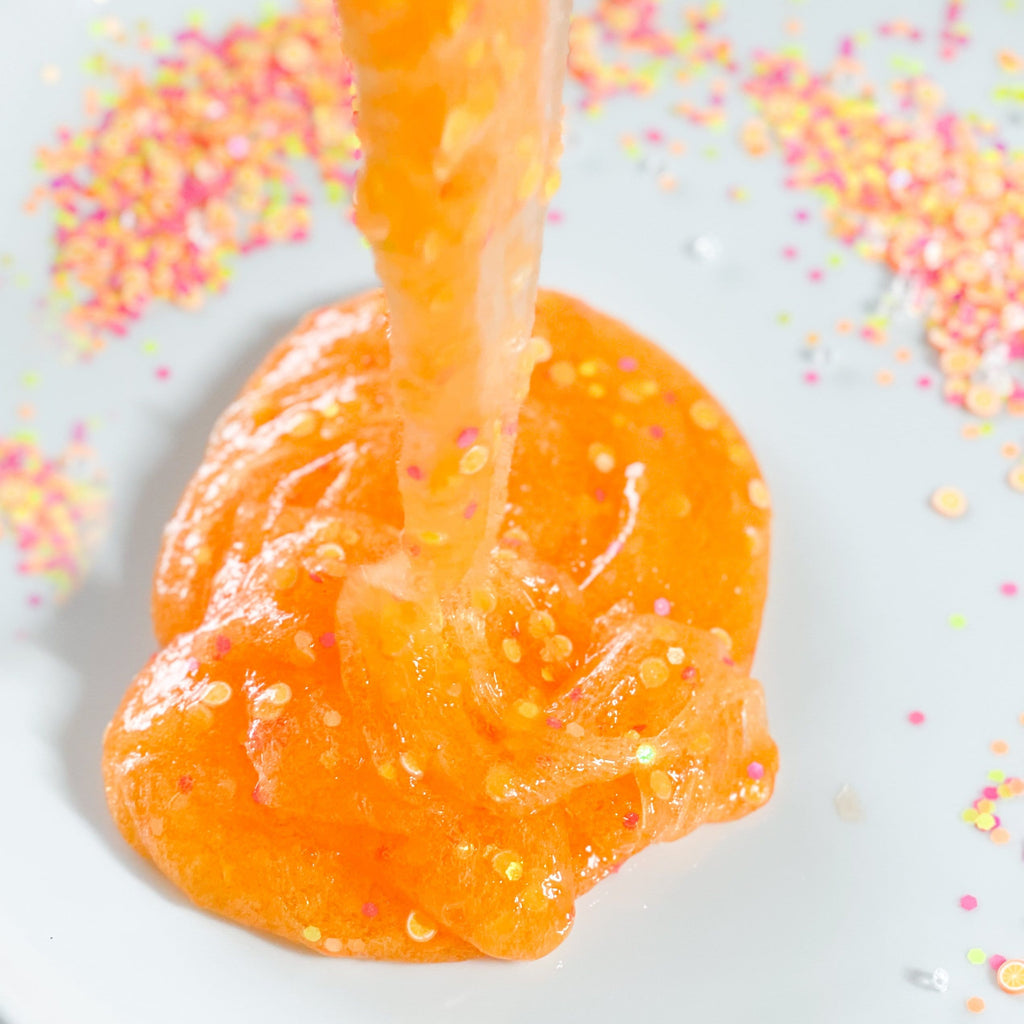 orange slime being pored onto a white plate with confetti for making the orange soda diy slime kit for kids